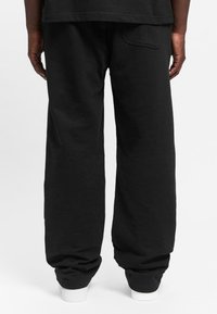 Black sweatpants made of soft fabric, featuring a relaxed fit, elastic cuffs, and a back pocket. The hem has a white accent band.