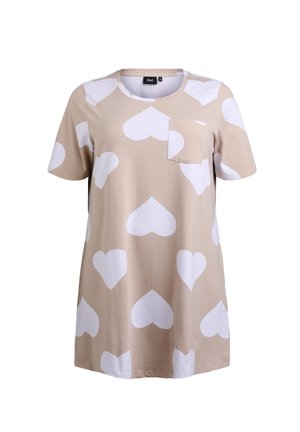 Beige t-shirt med kort ärm och rundad halsringning, med stora vita hjärtformade mönster och en liten bröstficka. Mjuk och slät tyg.