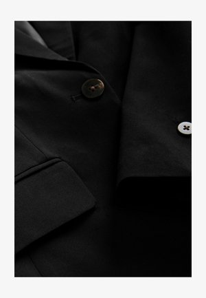 Sort blazer lavet af glat stof med et notched krave, der har to knapper – én mørk, én lys – og en flaplomme detalje.