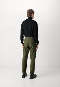 Camisa preta de mangas longas e calças cargo verdes-oliva com bolsos laterais. As calças têm um ajuste afunilado e punhos elásticos, complementadas por sapatos pretos.