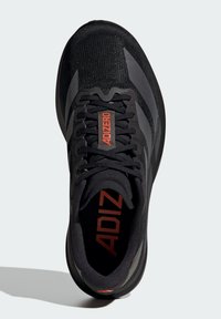 Zapatilla deportiva negra con parte superior de punto, con detalles en naranja, cordones planos y un diseño aerodinámico. Branding minimalista mostrado.