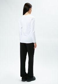 Langärmliges weißes Oberteil, kombiniert mit schwarzen, weiten Hosen. Das Outfit zeichnet sich durch ein einfaches, klares Design ohne sichtbare Muster oder Akzente aus.