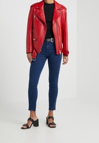 Red leather biker jacket with silver hardware, black ribbed top, blue high-waisted skinny jeans with frayed hem, and black block-heeled sandals.