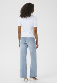 Weißes ribbeltes Kurzarmoberteil, kombiniert mit hellblauen weitem Jeans. Die Jeans verfügen über ein klassisches Fünf-Taschen-Design und subtile Nähte.