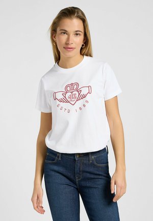 Weißes Baumwoll-T-Shirt mit einem roten grafischen Design von Händen und einem Herz, runder Halsausschnitt und kurzen Ärmeln. Getragen mit dunkelblauen Jeans.