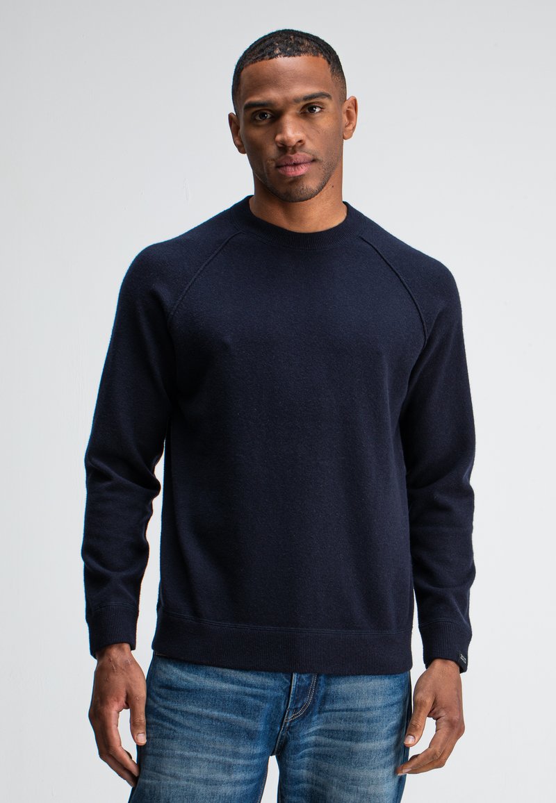 Marineblauwe crewneck sweater met ribgebreide manchetten en zoom, gemaakt van zachte, gestructureerde stof. Beschikt over raglanmouwen voor een ontspannen pasvorm.
