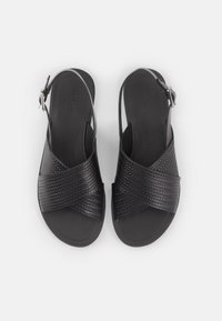 Μαύρες δερμάτινες σάντες με υφαντή υφή, διακεκριμένες από σχέδιο σταυρωτής διαμόρφωσης και ρυθμιζόμενη αλυσίδα αστραγάλου με μέταλλο κούμπωμα.