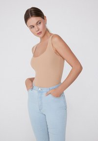 Béžový body s tenkými ramínky, kulatým výstřihem a hladkým materiálem; spárováno se světle modrými džíny s vysokým pasem a předními kapsami.