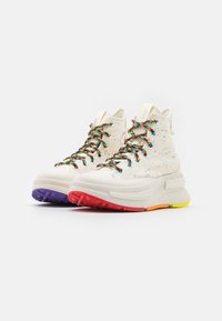 High-top sneakers with a speckled white upper, multicolored laces, and vibrant rubber outsoles in red, purple, orange, and yellow accents.