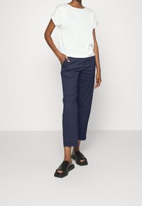 Haut blanc à manches courtes, pantalon court bleu marine et sandales plates noires. Tissu lisse, coupe décontractée et design ouvert avec une semelle épaisse.