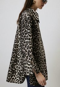 Leren shirt met luipaardprint in zwart en beige, voorzien van een kraag, lange mouwen en zijsplitten. Gemaakt van zacht materiaal met een comfortabele pasvorm.