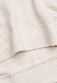 Tessuto beige, texture morbida e leggermente rigata. Presenta un orlo liscio e sottili variazioni di colore in tutto il tessuto.