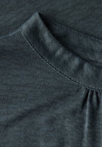 Tmavě šedá látka s jemnou strukturou. Kulatý výstřih s mírným nařasením. Hladký povrch, rovnoměrné šití podél okrajů.