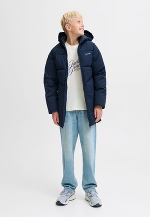 Tamsiai mėlyna pūkinė striukė su gobtuvu, su priekyje esančia užtrauktuku ir siuvinėta tekstūra. Derinama su šviesia marškinėlių palaidine ir laisvai krentančiomis šviesiomis džinsais.