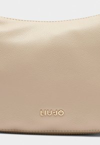 Beige Leder-Schultertasche mit strukturierter Oberfläche und goldfarbenem "LIU-JO"-Logo auf der Vorderseite in der Nähe des Reißverschlusses.