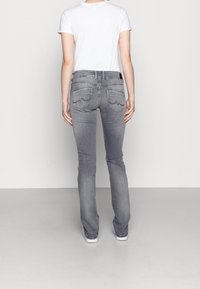 Jeans de mezclilla gris con un diseño de pierna recta, que cuentan con dos bolsillos traseros con costura curva, llevados con una camiseta blanca lisa y zapatillas blancas.