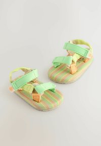 Grüne und orange Sandalen mit gestreiften Textilsohlen, ausgestattet mit verstellbaren Riemen und einer strukturierten Gummisohle. Leichtes Design.