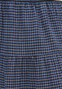 Tkanina w kratę w kolorach granatowym i niebieskim o miękkiej fakturze, z marszczonym stanem i dwuwarstwowym krojem. Pionowe i poziome linie tworzą wzór w kratkę.