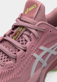 Ροζ αθλητικό παπούτσι ASICS με υφασμένο δίχτυ, ανοιχτοροζ κορδόνια, λευκό λογότυπο στο πλάι και νέον κίτρινη επωνυμία "asics" και "Court FF" στη γλώσσα και στην προστατευτική λωρίδα των κορδονιών.