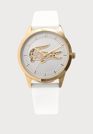 Goldene Uhr mit weißem Armband, die in der Mitte ein krokodilförmiges Design sowie goldene Stundenmarkierungen und Zeiger hat.