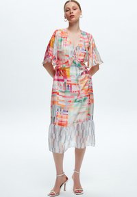 Robe multicolore, légère, avec des manches volantées, une taille à cordon de serrage et un ourlet froncé. Présente des motifs géométriques dans des teintes vives.
