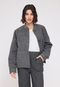 Gray felt jacket with a round neckline, button front, and long sleeves. It features a textured finish and is styled with gray trousers.
