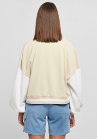 Světle krémová a bílá color-block svetr s volným střihem, spadlými rameny, žebrovaným lemem a měkkou texturou, spárovaný se světle modrými šortkami.