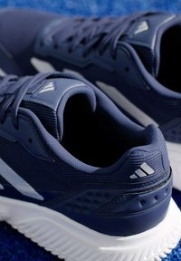 Morskie buty sportowe z teksturowaną cholewką, białą podeszwą i srebrnymi akcentami. Wśród cech znajdują się wzmocniony zapiętek i otwory wentylacyjne.