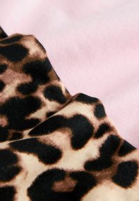 Tissu doux avec imprimé léopard beige et noir couvrant partiellement un fond textile lisse rose clair.