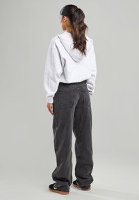 Harmaa huppari, jossa on suuri takahuppu, yhdessä löysien mustien farkkujen kanssa, joissa on taskupusseja, ja mustat liukuasit kengät, joissa on kumipohjat.