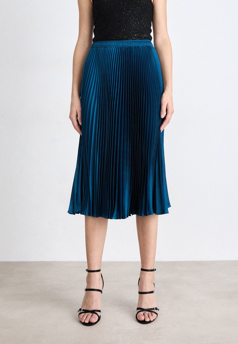 Gonna midi plissettata in teal realizzata in tessuto morbido, con vita aderente e silhouette fluida. Sandali neri con tacchi a stiletto completano il look.