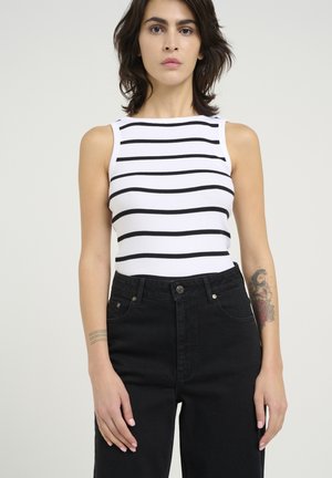 Vit ärmlös topp med svarta horisontella ränder, i kombination med högmidjade svarta jeans. Utmärkande tatuering på armen. Enkelt mönster, avslappnad stil.