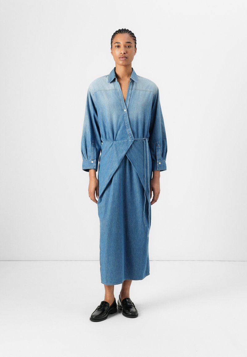 Denim skjortekjole med lange ermer, knappestolpe foran og omslagdesignet. Lys til mørk blå gradient, glatt tekstur og ankellengde.