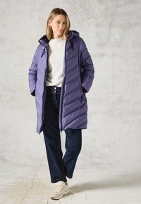 Fialová péřová bunda s kapucí, s prošívaným designem a zipovým uzávěrem. Nositá přes lehký svetr a námořnické džíny, v kombinaci s teniskami.