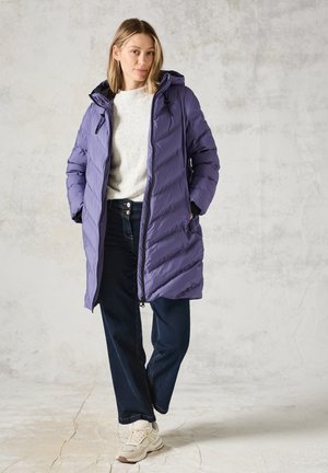 Giacca a vento viola con cappuccio, caratterizzata da un design trapuntato e chiusura con zip. Indossata sopra un maglione leggero e jeans blu scuro, abbinata a sneakers.
