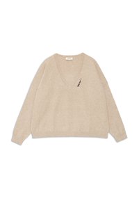Beige V-hals trui van zacht materiaal met verlaagde schouders en een decoratieve speld aan de voorkant links. Lange mouwen en een relaxte pasvorm.