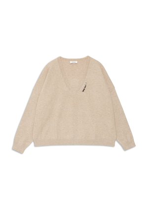 Pull beige en V fabriqué en tissu doux avec des épaules tombantes et une épingle décorative sur le côté gauche devant. Manches longues et coupe décontractée.