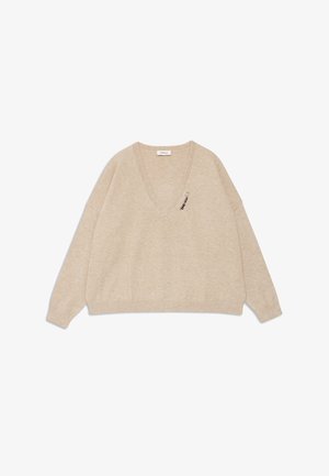 Maglione beige a V in morbido tessuto con spalle scese e una spilla decorativa sul lato sinistro. Maniche lunghe e vestibilità rilassata.