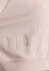 Brassière de sport rose clair en tissu texturé, avec un motif de logo en relief sur le devant et une bande élastique lisse en dessous.