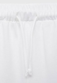 Pantaloni de trening albi din bumbac cu un elastic în talie și șnururi albe, având o textură moale și un design minimalist.