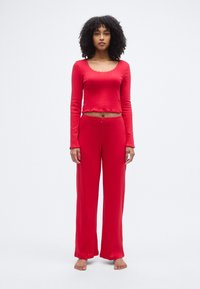 Haut rouge à manches longues avec des bords festonnés, associé à un pantalon rouge ample avec une taille réglable à cordon.
