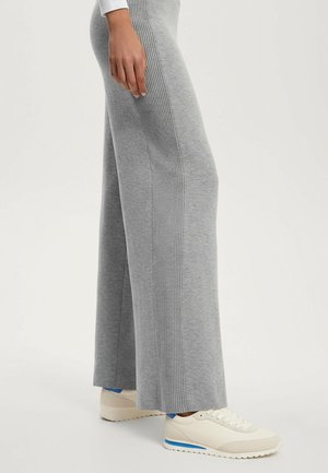 Grå vidde bukser med ribbet sidestykke, lavet af blødt stof. Kombineret med cremefarvede sneakers med en blå accentstribe.