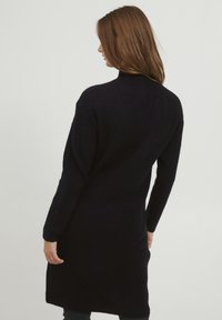 Abito maglione nero a maglia con maniche lunghe, collo alto e texture a costine, che scende sotto i fianchi, mostrando un design semplice e pulito.