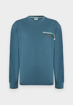 Kékeszöld hosszú ujjú, kerek nyakú pulóver cipzáros mellzsebbel és Columbia logóval ellátott folttal, világosszürke háttéren.