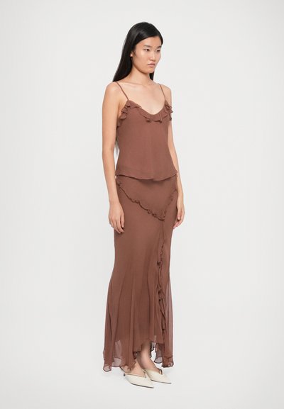 Brown dress with ruffled accents at neckline and hem. Lightweight fabric with a flowing silhouette. Styled with pointed toe shoes.