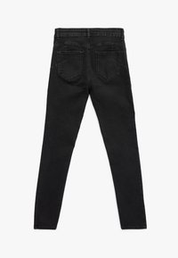 Jeans negros ajustados extendidos mostrando la parte trasera con dos bolsillos y trabillas en la cintura.