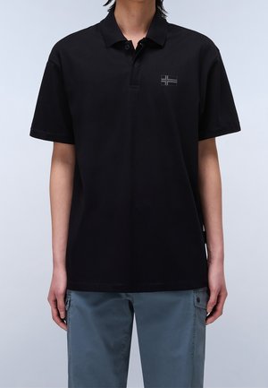 Schwarzes Poloshirt mit klassischem Kragen, kurzen Ärmeln und einem kleinen dunklen Emblem. Dazu hellgraue Cargo-Hosen.