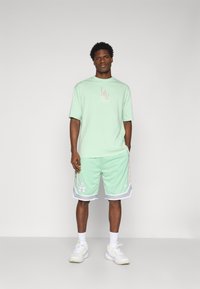 Mint green short-sleeve t-shirt with LA logo. Paired with mesh shorts featuring white trim and patterned side accents. White sneakers.