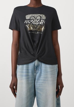Schwarzes kurzärmeliges T-Shirt mit Knoten vorne, Animal-Print-Streifen, einer Herzumrandung und dem Text „Always keep a wild heart“, getragen zu hellblauen Jeans.