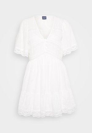 Witte jurk met een V-hals, korte pofmouwen, knopen aan de voorkant en een kanten rand van oogjes. Heeft een gelaagde rok en een gestructureerde stof.